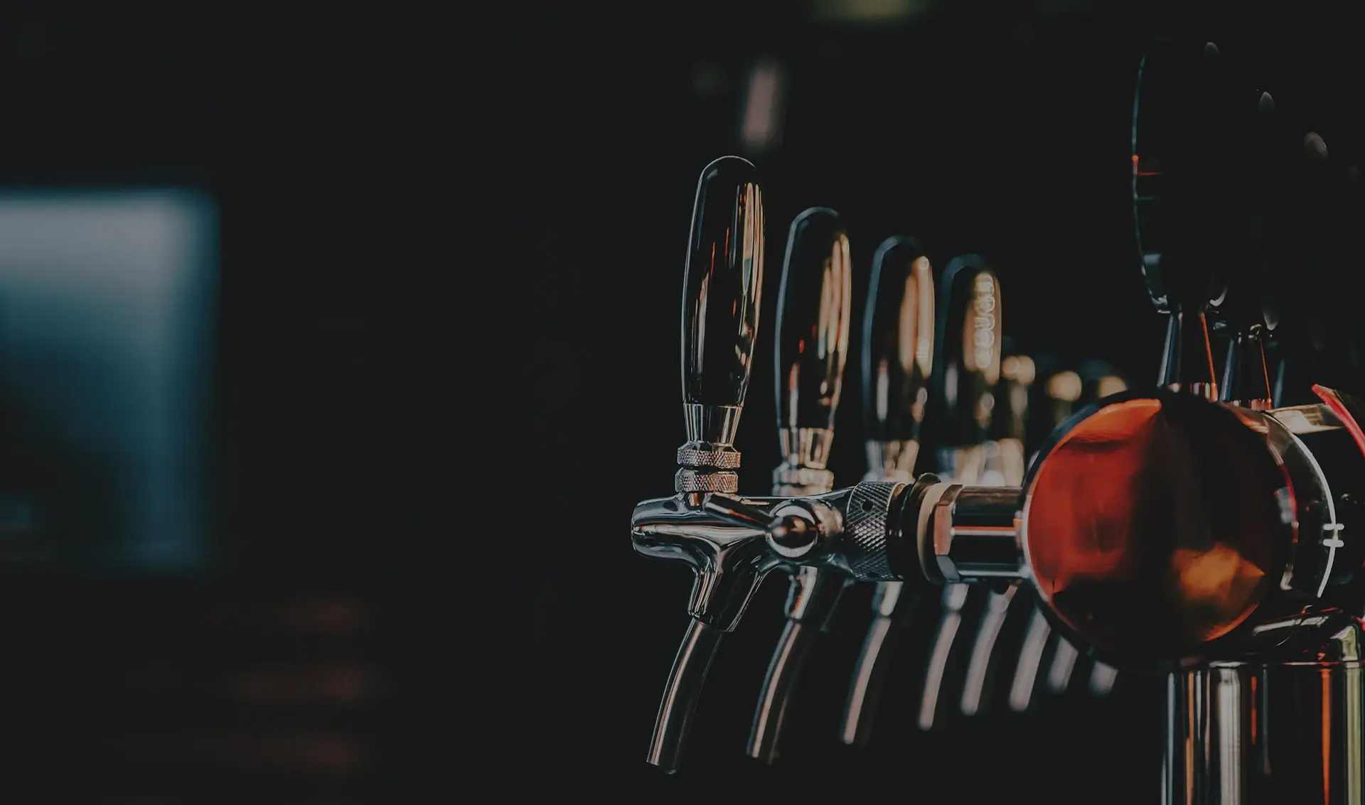 A row of metallic beer taps is displayed, highlighted by ambient lighting.
