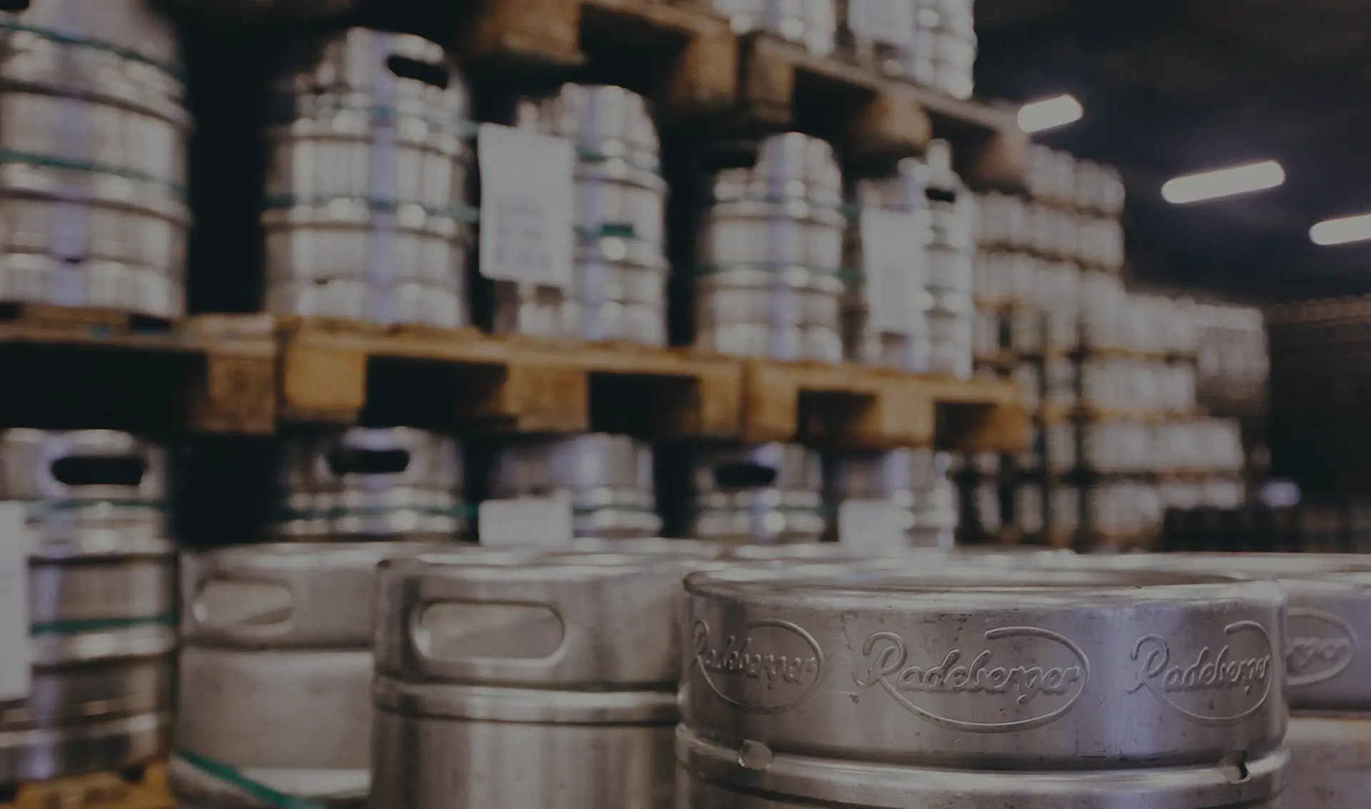 Several metal beer kegs are stacked in a storage area, each marked with embossed branding.