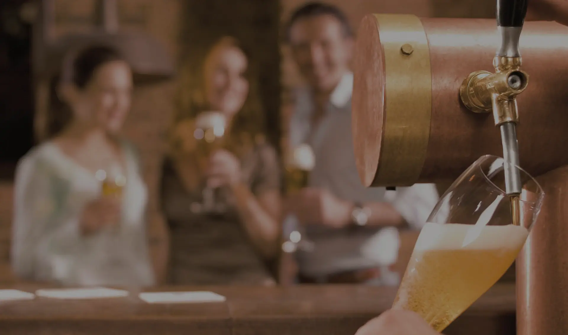 A person fills a glass with beer from a tap, with smiling friends in the background.