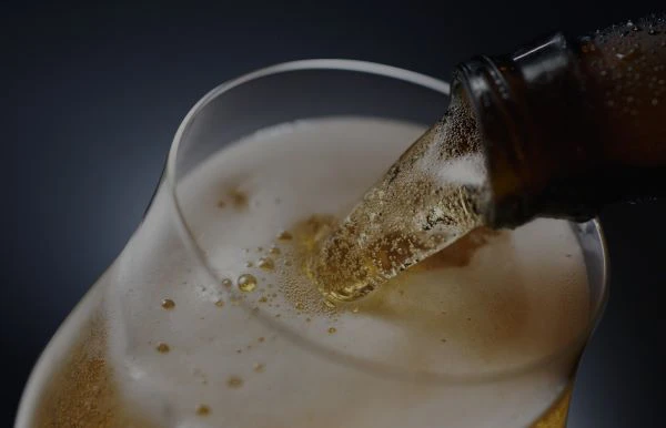 Beer is being poured from a bottle into a glass, creating foam at the top.